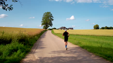 Following-a-running-man-closely-from-behind---a-deserted-asphalt-path-between-ripening-fields-and-the-embrace-of-nature---drone-shot