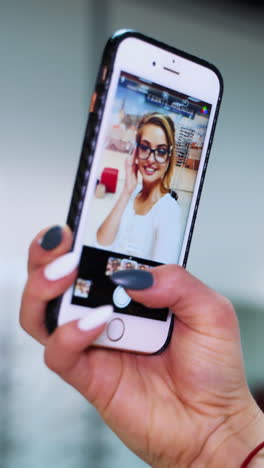 woman looks at herself in the mobile phone. female's hand holding phone and showing the video with a beautiful woman in eyeglasses. vertical video
