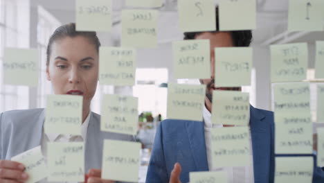 corporate business team using sticky notes brainstorming problem solving strategy on glass whiteboard thinking of solution for project deadline in office