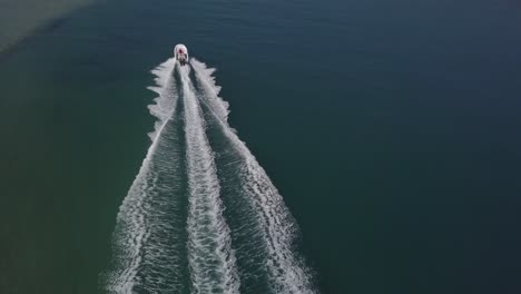 chase aerial as white speed boat splashes wake in shallow green lagoon