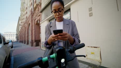 young woman using a smartphone near electric scooter in the city