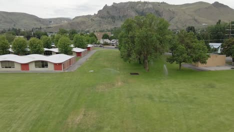 The-Beautiful-Town-View-Surrounded-With-Green-Grassland-And-Trees-In-Background-Of-High-Mountains-Under-The-Bright-Cloudy-Sky---Wide-Shot