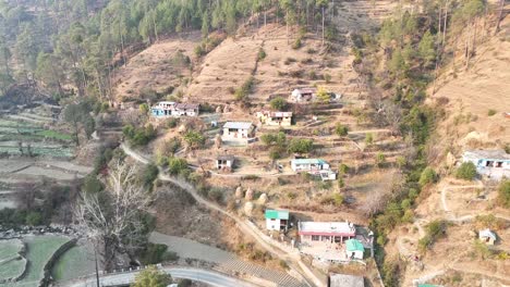 aerial drone footage showcasing houses scattered across dry agricultural hill on sunny day, with golden brown land highlighting the rural landscape in india