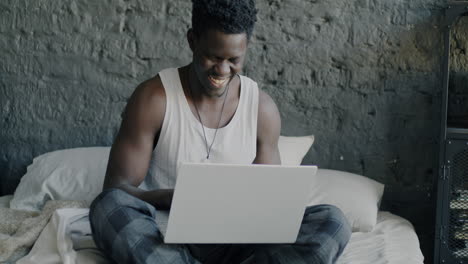happy man working on laptop in bed
