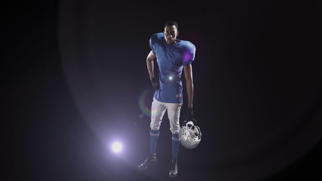Holding helmet, American football player in blue uniform standing under spotlight