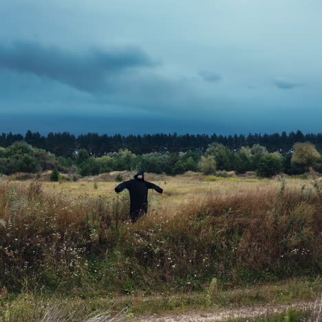 dark scary figure on the field. black death in mantle standing with outstretched arms among summer field under evening sky.