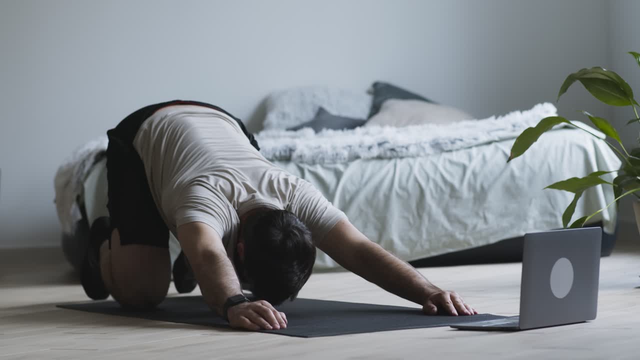 집에서 노트북 앞에서 요가 또는 스트레칭 운동을 하는 남자