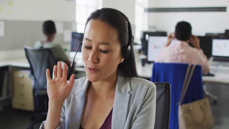 feliz mujer de negocios asiática sentada en el escritorio usando computadora y hablando en auriculares