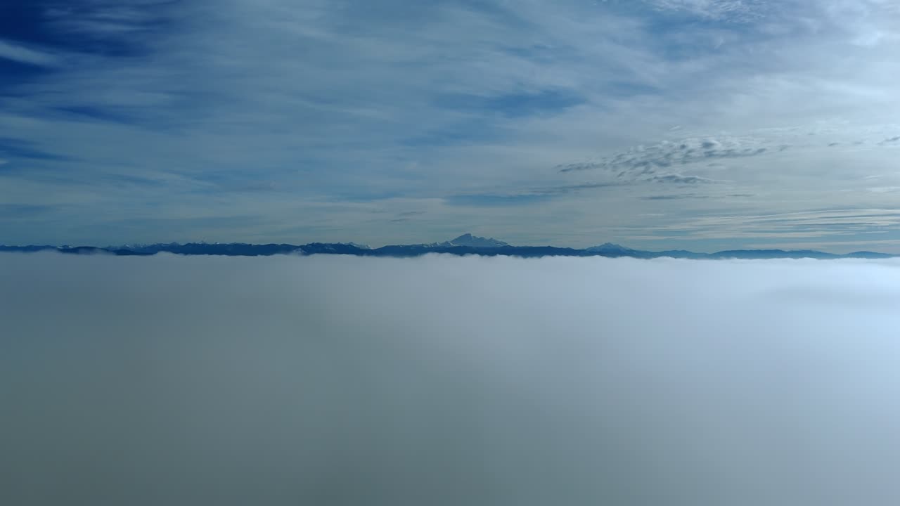 カナダ、ブリティッシュコロンビア州ラングリー – 青い空の下に広がる広大な雲の層と、遠くの地平線に見える山々のシルエット – ドローン空撮