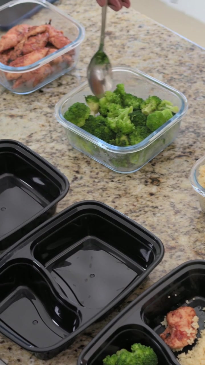 Vertical video: Arm scooping broccoli adding chicken on kitchen counter with empty trays and spoon