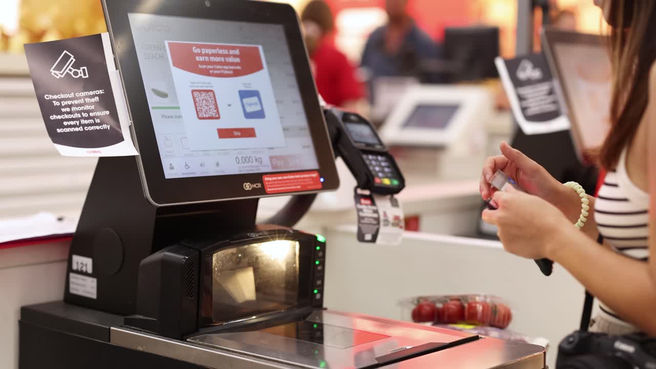 A customer uses a self-checkout machine for cashless payment in a well-lit retail environment on the Gold Coast