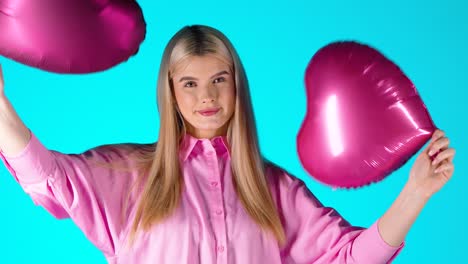 una mujer rubia muy bonita agitando globos púrpura en forma de corazón y luego los lanza, una toma de estudio colorida