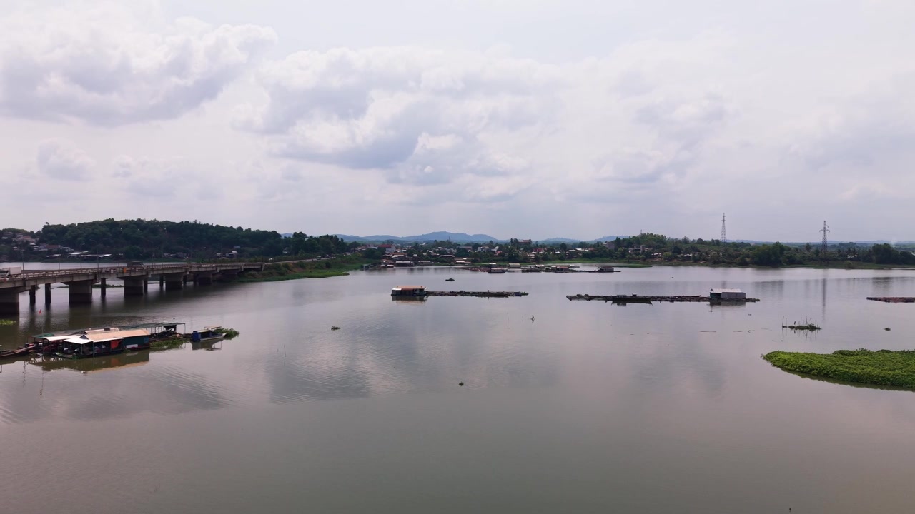 Il ponte La Nga si estende sul fiume a Dong Nai, Vietnam. Barche lungo l'acqua, mentre la vegetazione circonda l'area. Le nuvole passano in alto, creando una vista del paesaggio.