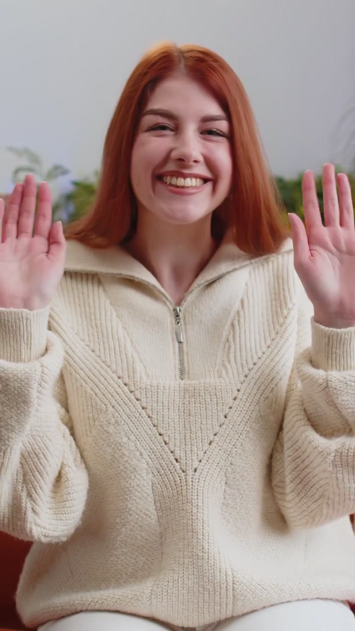 Donna carina che sorride amichevolmente alla telecamera, agita le mani, fa un gesto, saluta, saluta a casa sul divano.