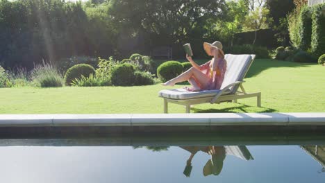 Mujer-Caucásica-Leyendo-Un-Libro-Mientras-Toma-El-Sol-En-Una-Tumbona-En-El-Jardín.