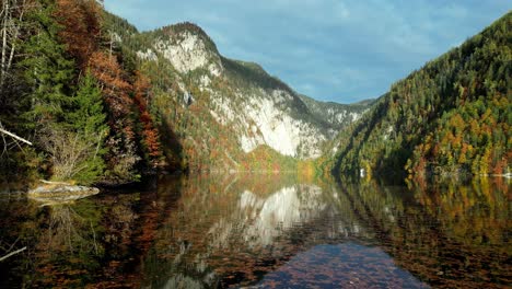 Autumn's-fiery-embrace-paints-the-mountains-around-a-tranquil-lake,-where-colorful-leaves-pirouette-on-the-water's-surface