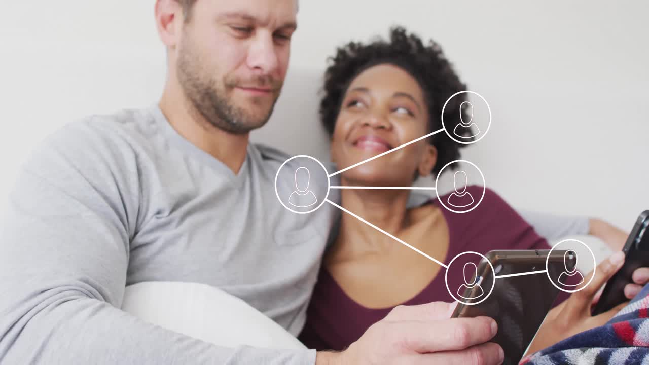 Couple tapping mobile devices on couch forming animated social network icons showing connection