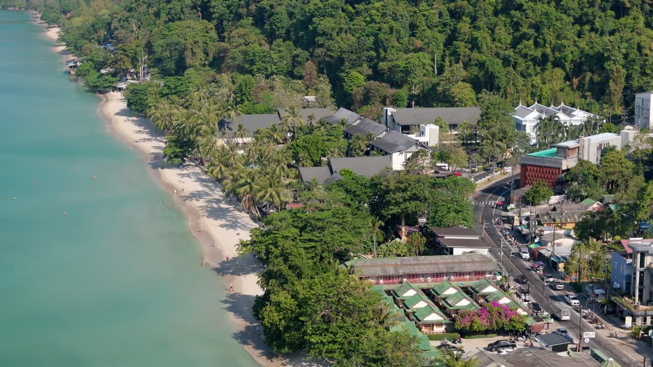 Flyover drone shot of Koh Chang's White Sand Beach, Thailand. Sunny morning over the village, sea, and lush greenery