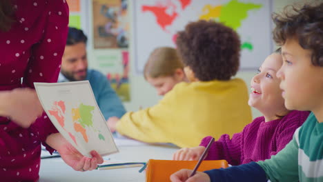 group of multi-cultural students putting hands up to answer question in classroom geography lesson