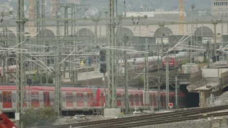 Busy-railway-station-with-multiple-trains,-urban-backdrop,-and-intricate-network-of-tracks-and-overhead-lines