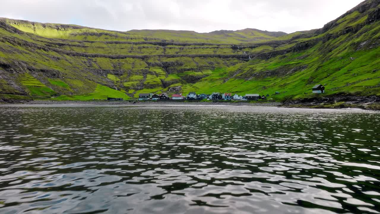 A calm village nestled between lush green cliffs in the Faroe Islands, seen from water