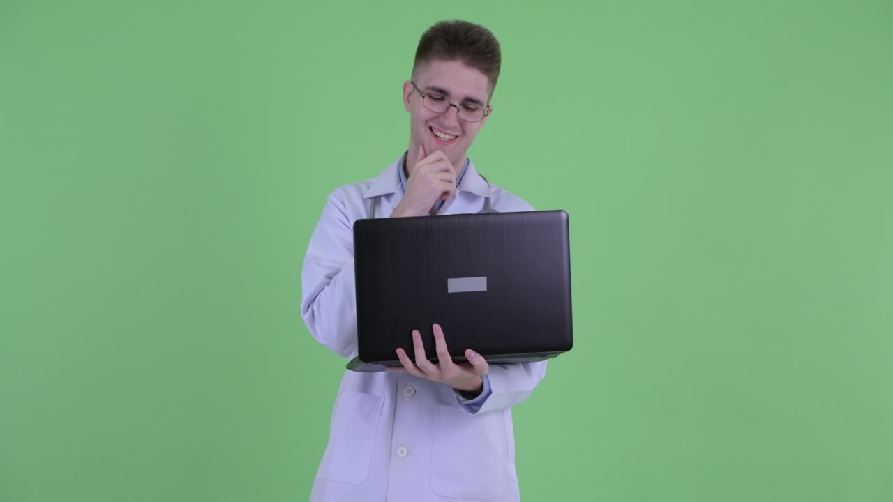 fotografía de estudio de un joven médico sonriendo y usando una computadora portátil contra un fondo de pantalla verde