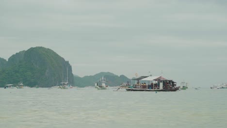 A-group-of-people-enjoying-a-boat-ride-on-traditional-wooden-tourist-boat-in-El-Nido,-Philippines-with-mountains-in-the-background---Wide-shot