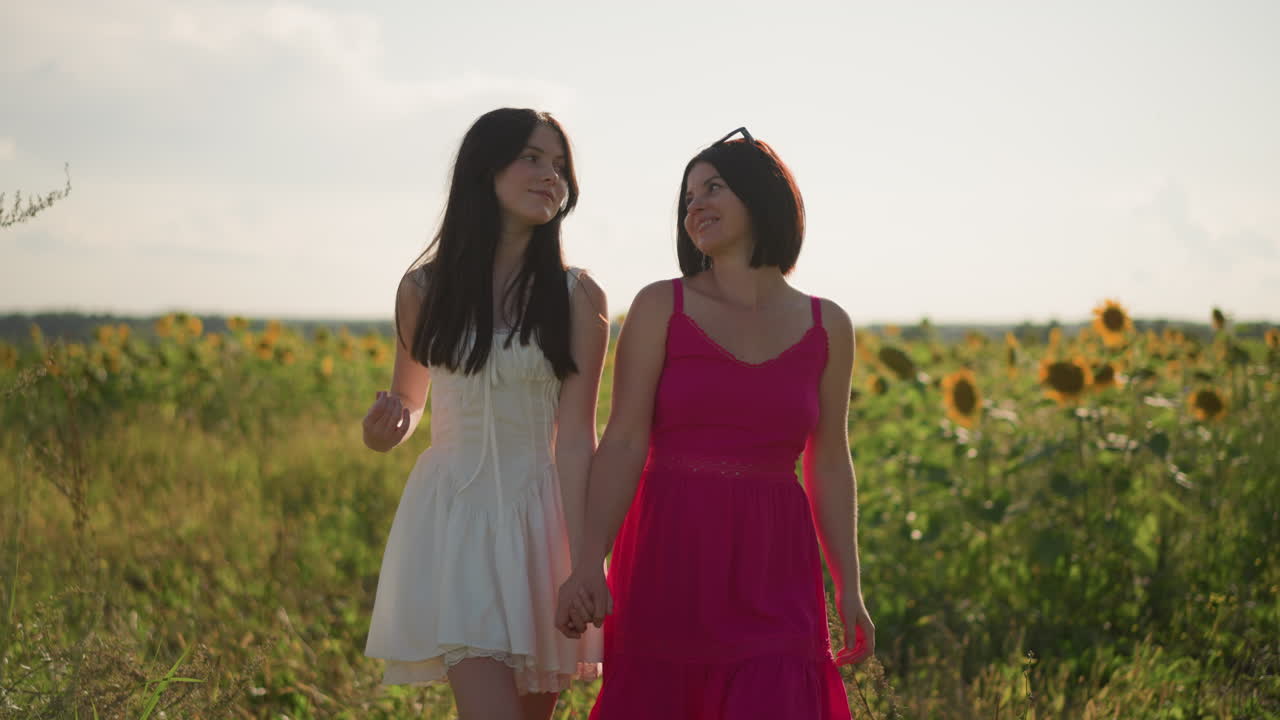 Happy friends outdoors, Two women laughing together in lively summer scene with sunflowers, Two friends enjoying carefree afternoon walking through field of sunflowers and smiling broadly