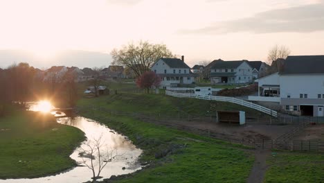 sun reflects in stream in meadow beside amish farm buildings