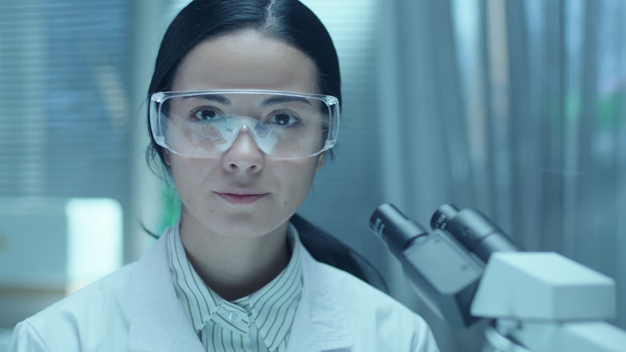Portrait of Female Scientist in Safety Glasses and Lab Coat beside Microscope