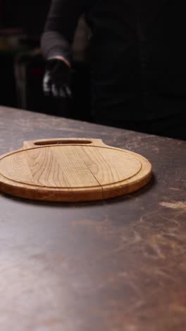 chef placing a round wooden cutting board on a dark kitchen counter