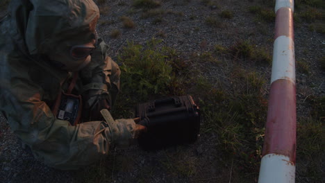 soldado con traje protector comprueba la radiación de un maletín sospechoso en la barrera