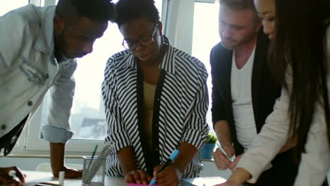 businesswoman in eyeglasses and striped shirt is standing explaining a project to her colleagues in the office