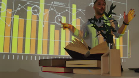 primer plano de los libros de texto en el escritorio mientras el maestro da una lección de matemáticas o ciencias en la escuela de pie en la parte delantera de la clase con la proyección de un gráfico
