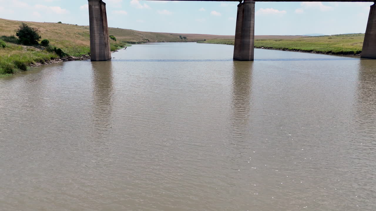 Tiefe Luftaufnahme über einem Fluss mit hochgeschwenktem Blick auf eine stillgelegte Eisenbahnbrücke.