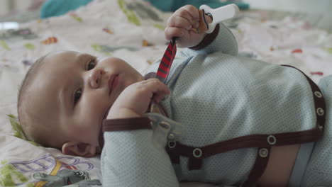 a four months old baby, lies on the coach with colorful bedsheet and playing with the baby's dummy toys, holding it in his hands