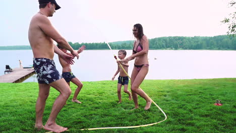 mother with father and two children playing on the lawn pouring water laughing and having fun on the playground with lawn on the background of his house near the lake in slow motion