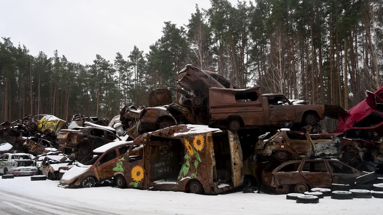 On a winter day in Irpin, Ukraine, a pile of burnt and destroyed cars is stacked together, with one vehicle painted with sunflower drawings, after intense battles between Ukrainian and Russian forces.