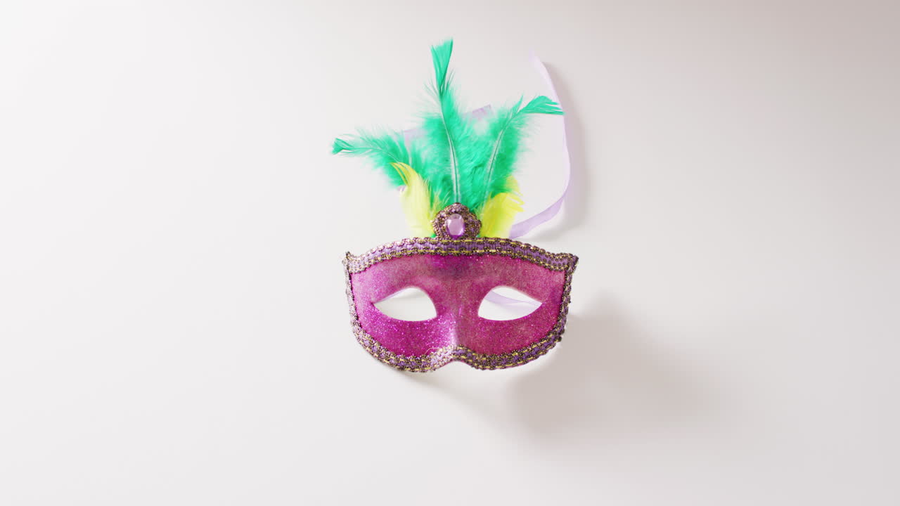 Video di maschera di carnevale rosa con piume verdi e gialle su sfondo bianco con spazio per il testo