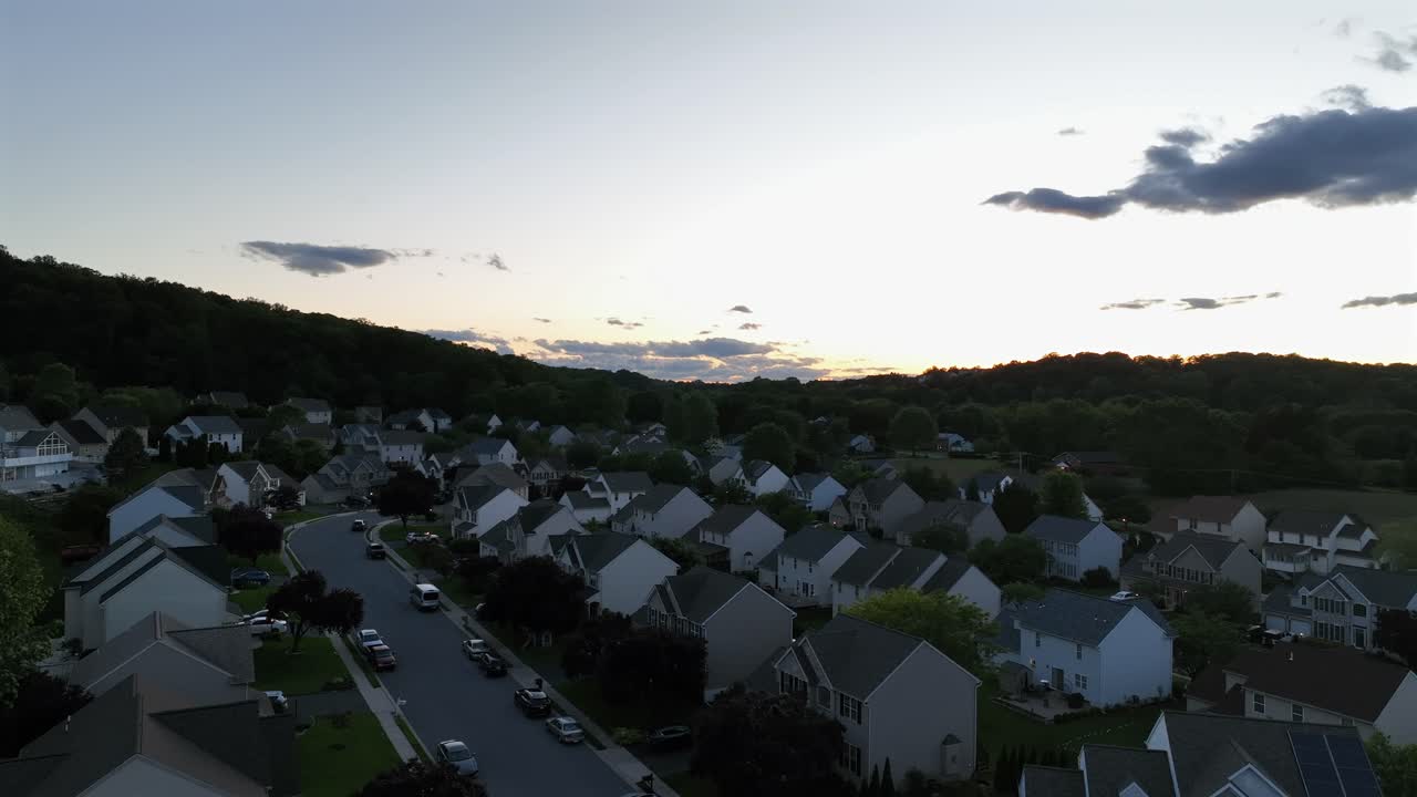 Single family houses with white facade and grey roof and parking cars on street. Dusk scene in american suburb. Descend drone wide shot. Calm and quiet vibes in spring.