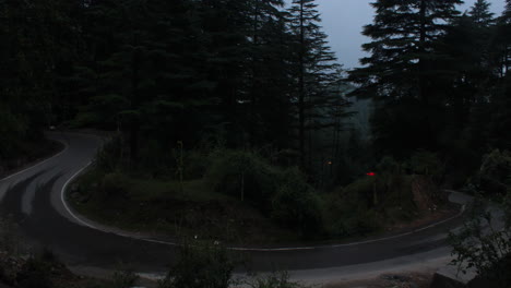 day to night timelpase of vehicles on a curved road in a forest
