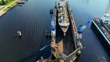 large ship under repair in dry dock with cranes, aerial view