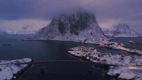 hamnøy lofoten in the foggy evening light with snow-covered houses and a sky overcast with dark clouds flying away