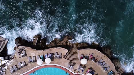 raised concrete boulevard with lounge beds on shore with waves crashing, top down