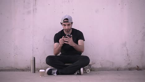 Young Man Sitting on a Skateboard, Using Smartphone