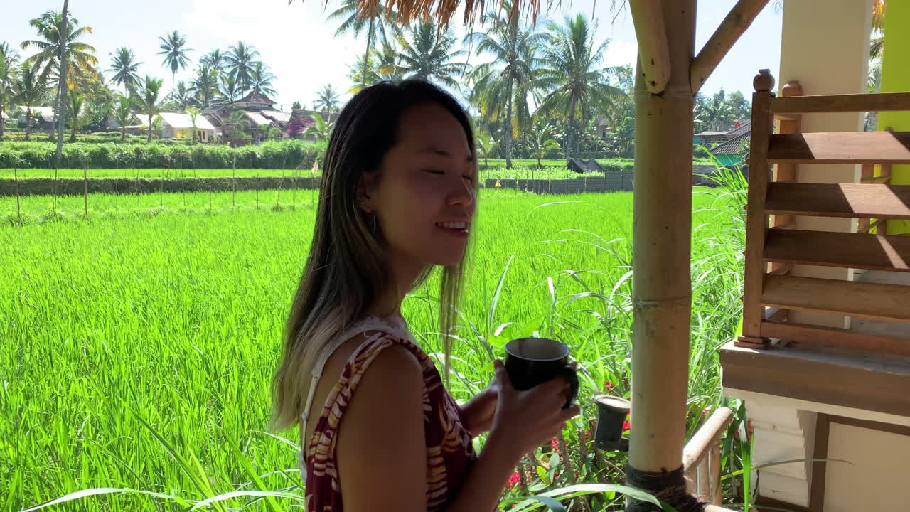 POV Walking Towards Female Tourist Enjoying Drink Sitting On Railing Looking Out To Green Lush Paddy Fields In Lombok