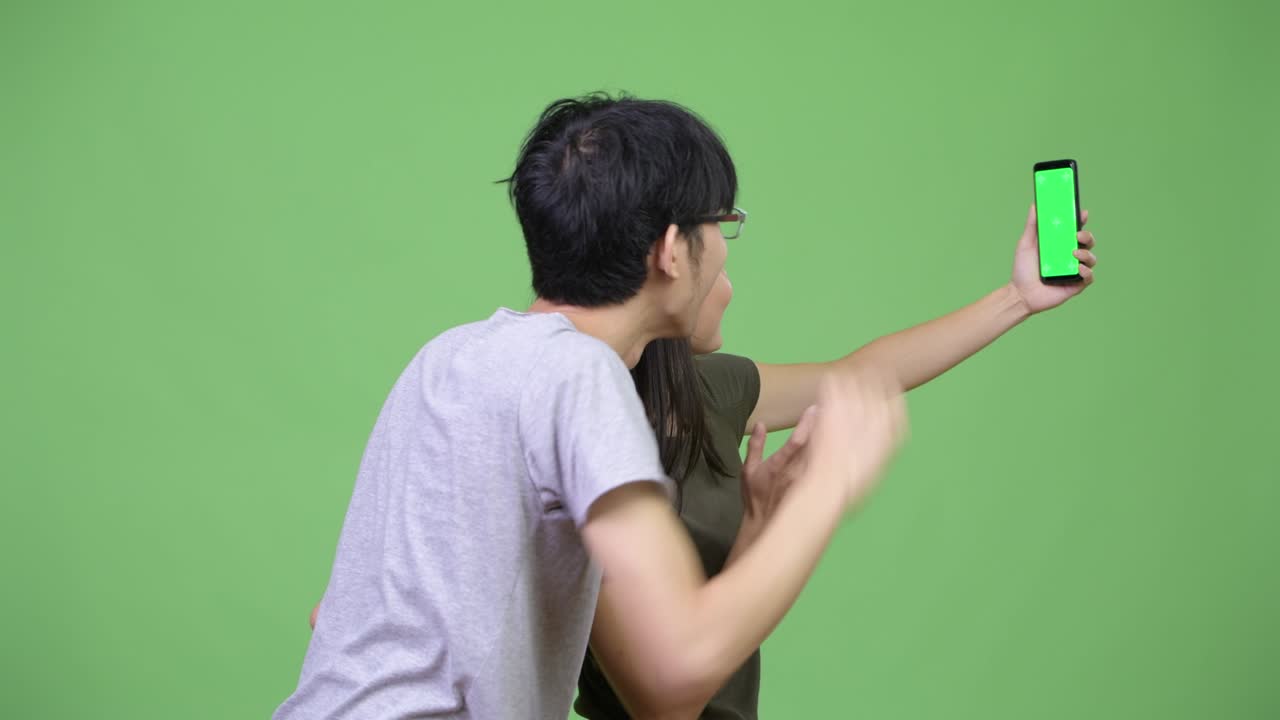 젊은 아시아 커플이 함께 전화를 보여주고 있습니다.