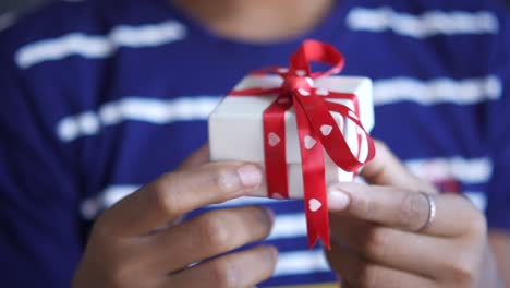 pequeña caja de regalo blanca con cinta roja en las manos