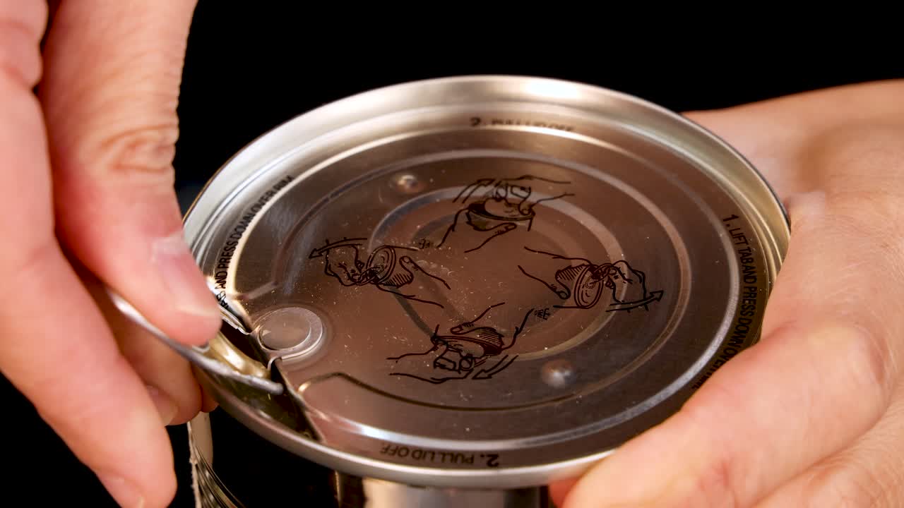 A close-up sequence shows a person’s hands opening a canned pineapple using a pull tab lid under bright, even lighting with a black background