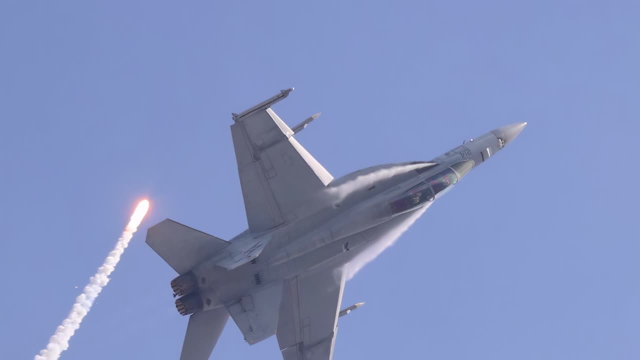 Close-up of an F/A-18 Hornet releasing flares during a steep climb against a clear blue sky.